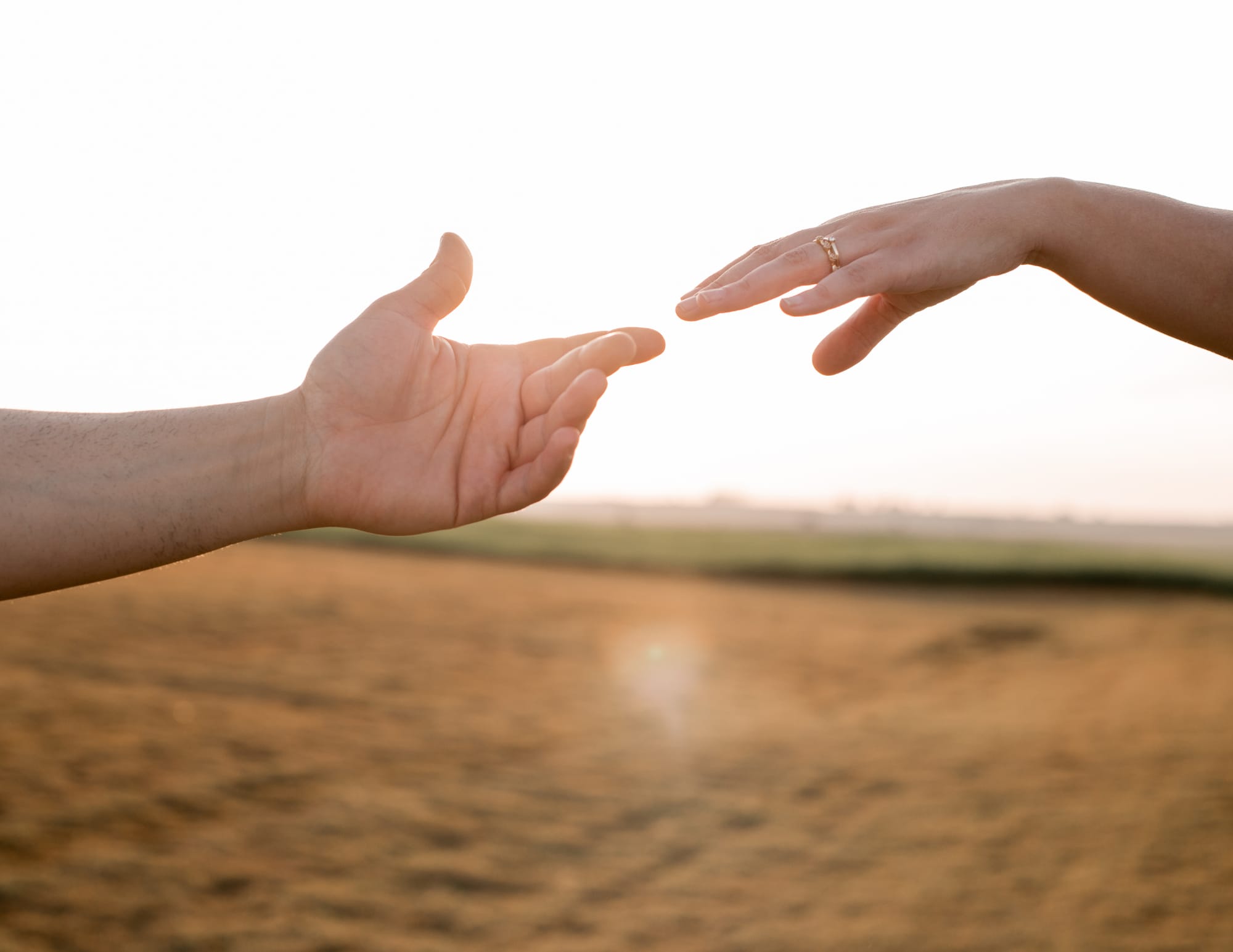 Mains se touchant presque sur fond de coucher de soleil, symbole du lien énergétique